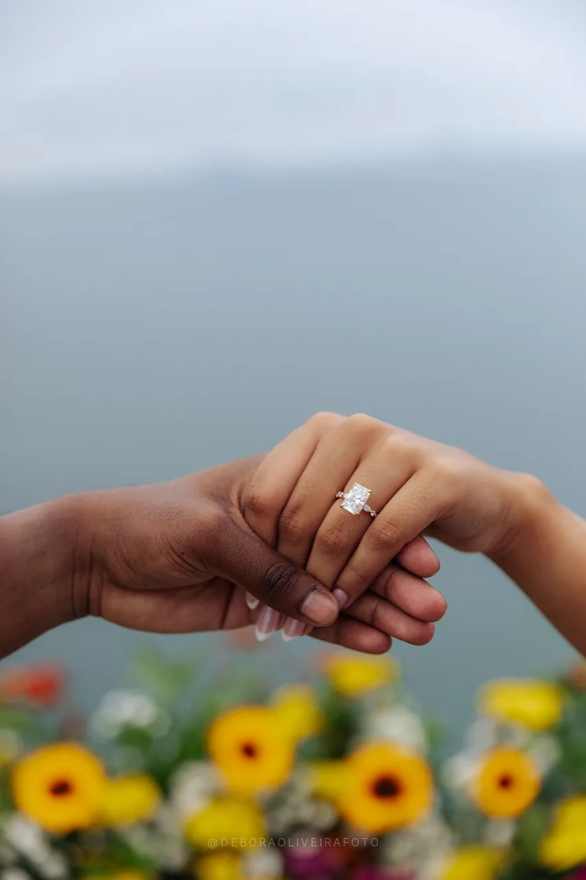 Manos tomadas con el anillo de compromiso y flores detrás en Río