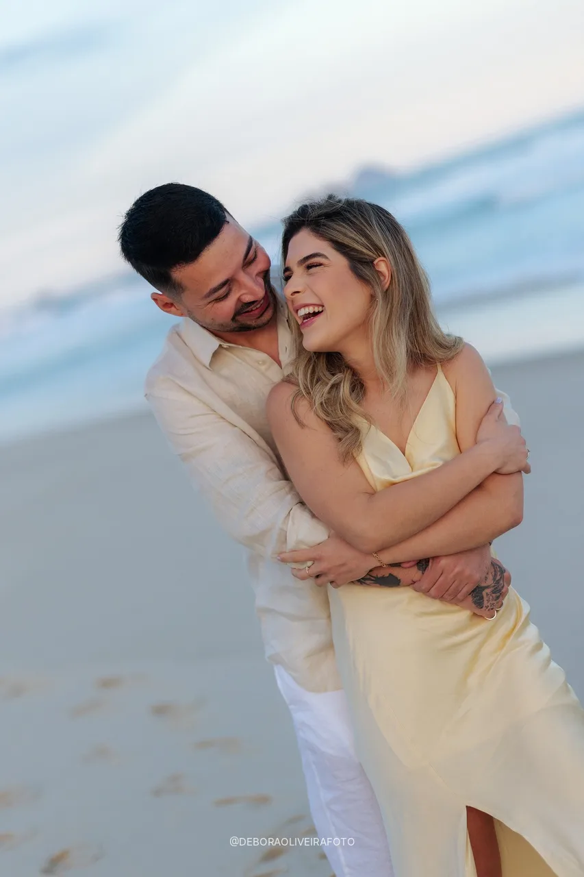 Isabely sorrindo no abraço de Eduardo na praia