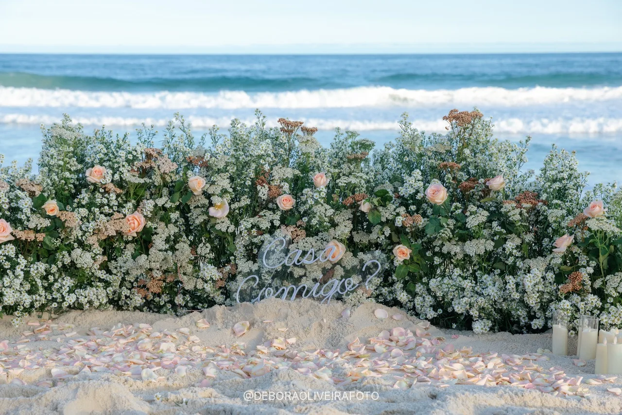Jardim de flores brancas e rosas com a placa Casa Comigo na praia
