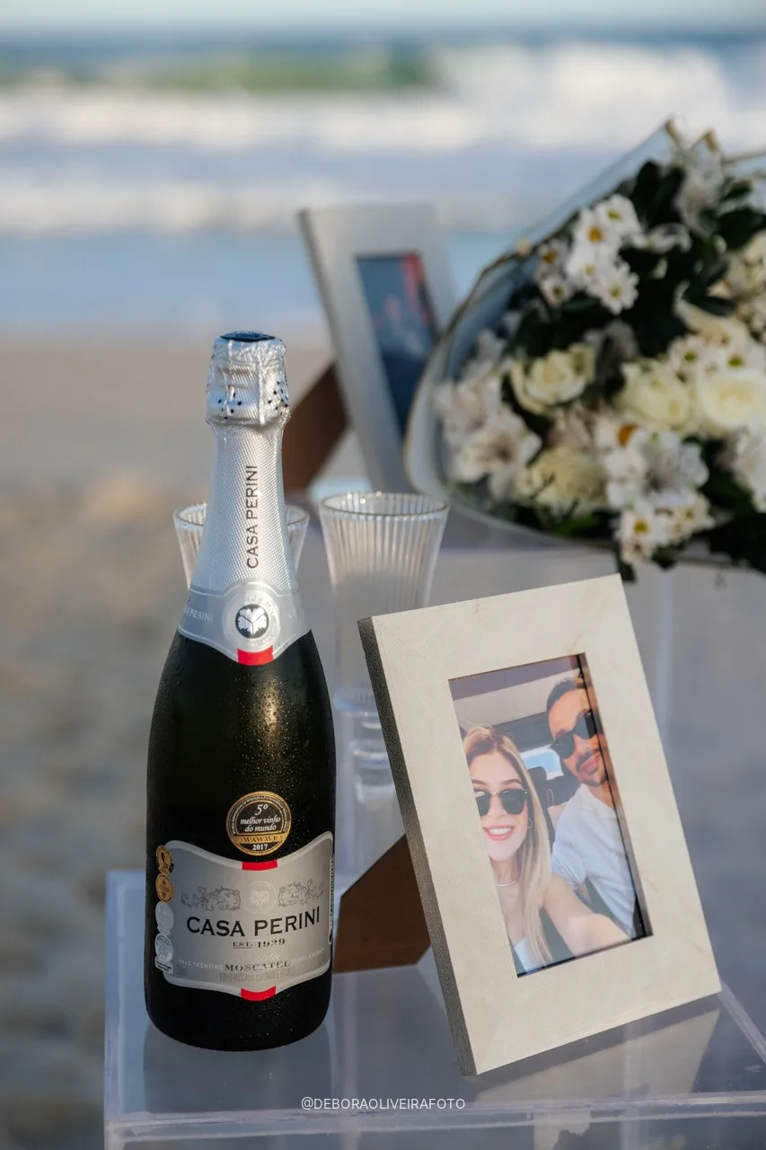 Espumante e porta-retrato do casal no suporte de acrílico do pedido na praia