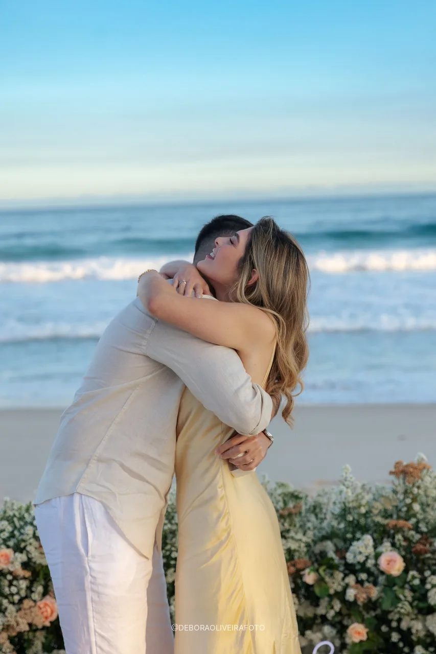 Casal noivo abraçado em frente às flores perto do mar