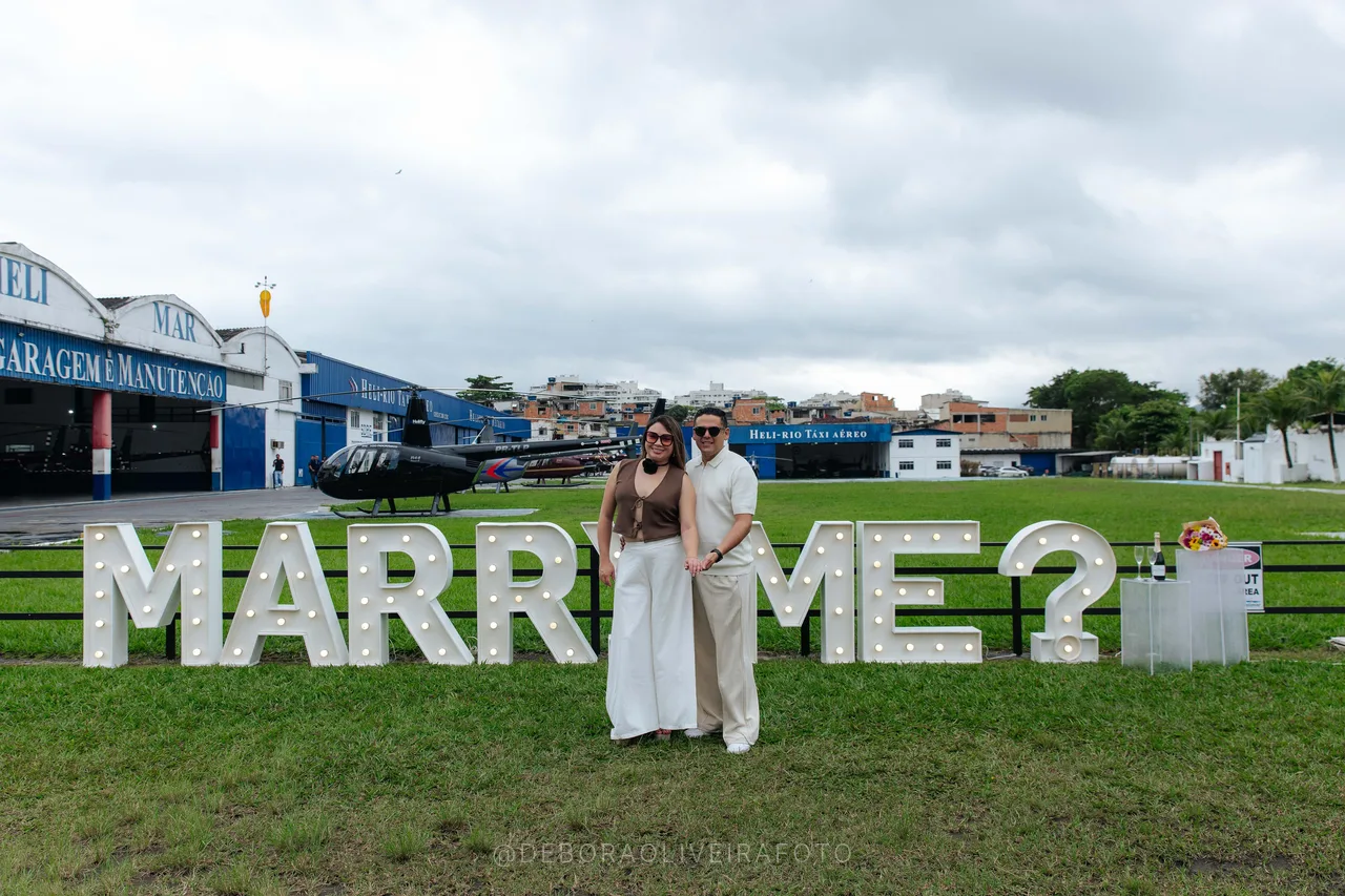 Engaged couple behind the lit Marry Me letters at a heliport in Rio
