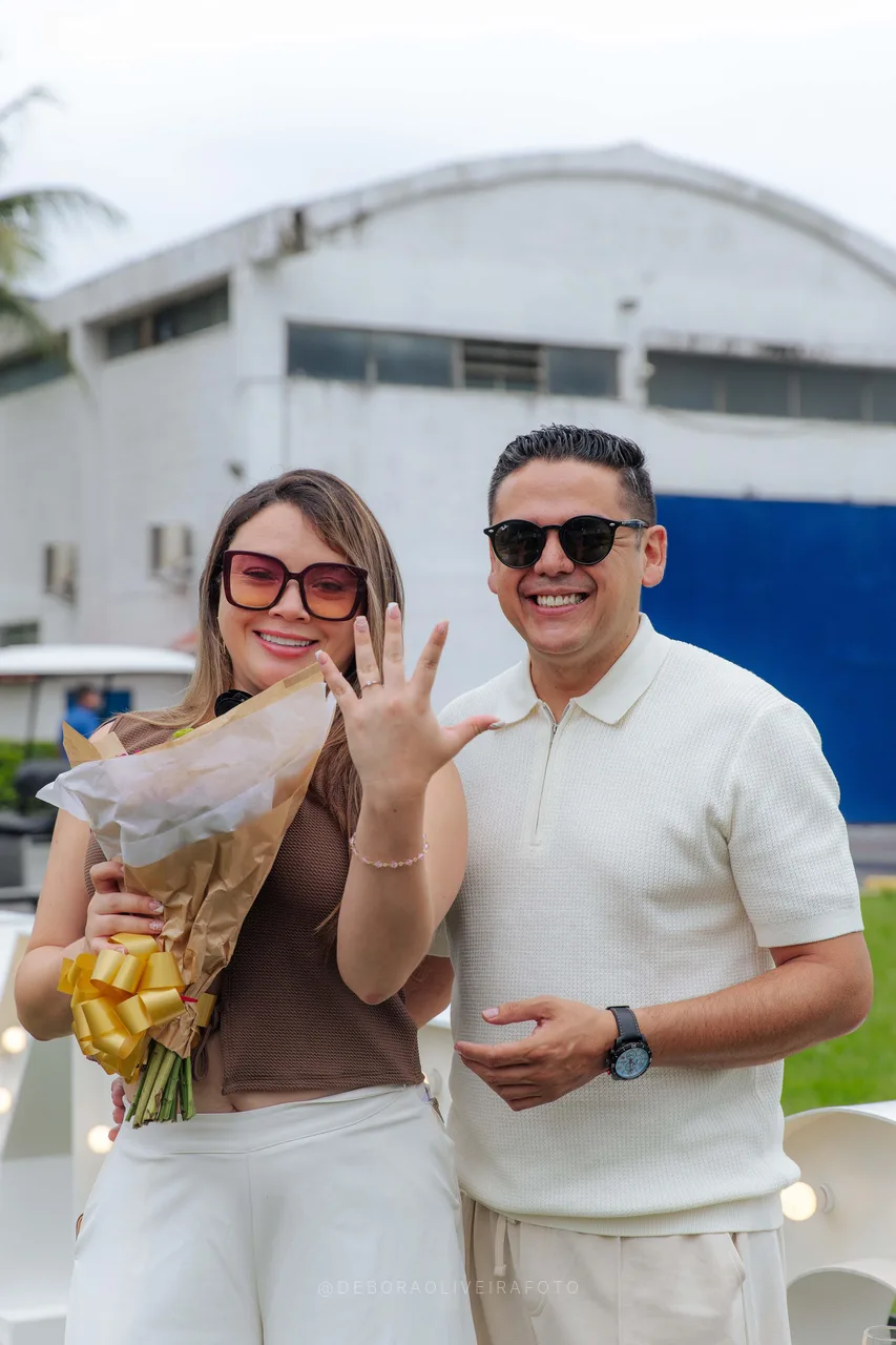 Andrea showing the engagement ring and flower bouquet next to the hangar