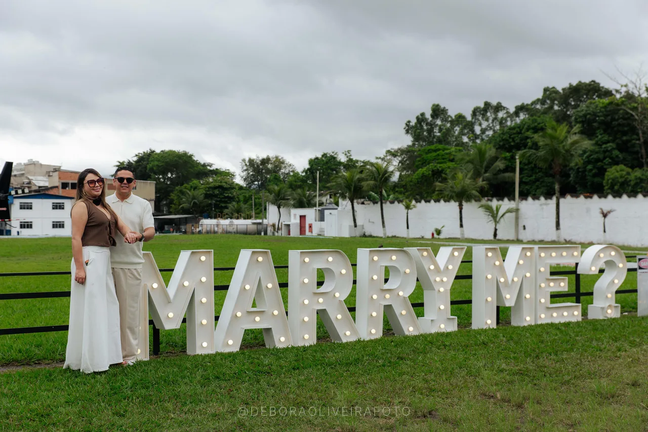 Engaged couple next to the lit Marry Me letters at the heliport