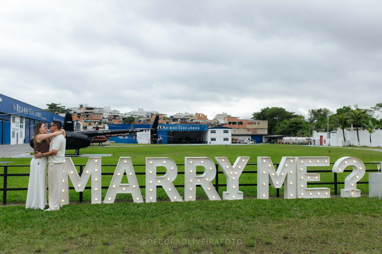 Heliport marriage proposal in Rio de Janeiro: Juan and Andrea embracing beside the Marry Me sign