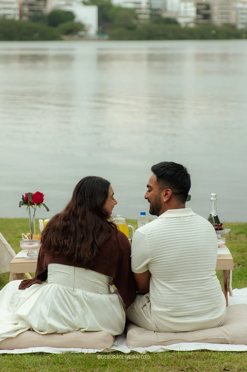 Naveen e Anisha sentados juntos no piquenique de frente para a Lagoa