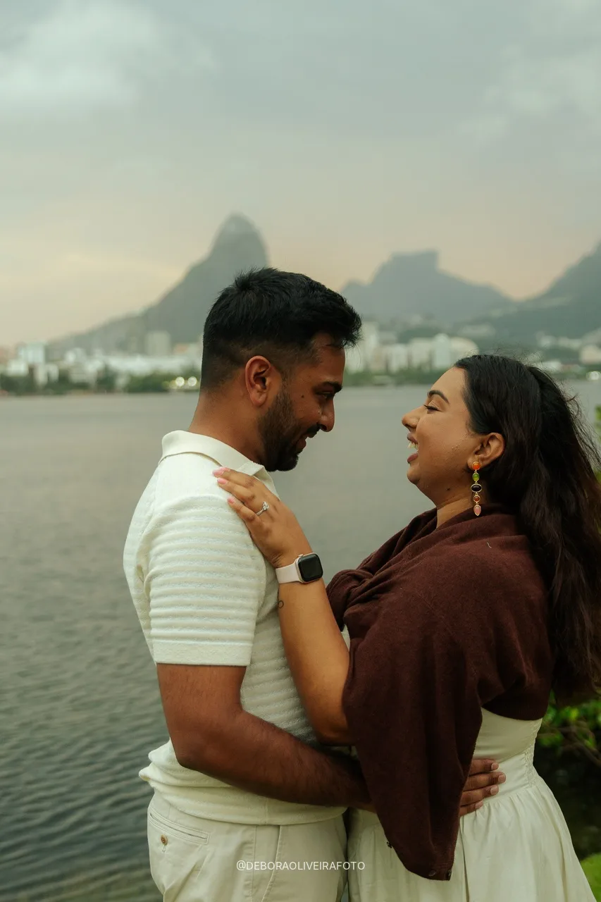 Naveen e Anisha sorrindo um para o outro na beira da água