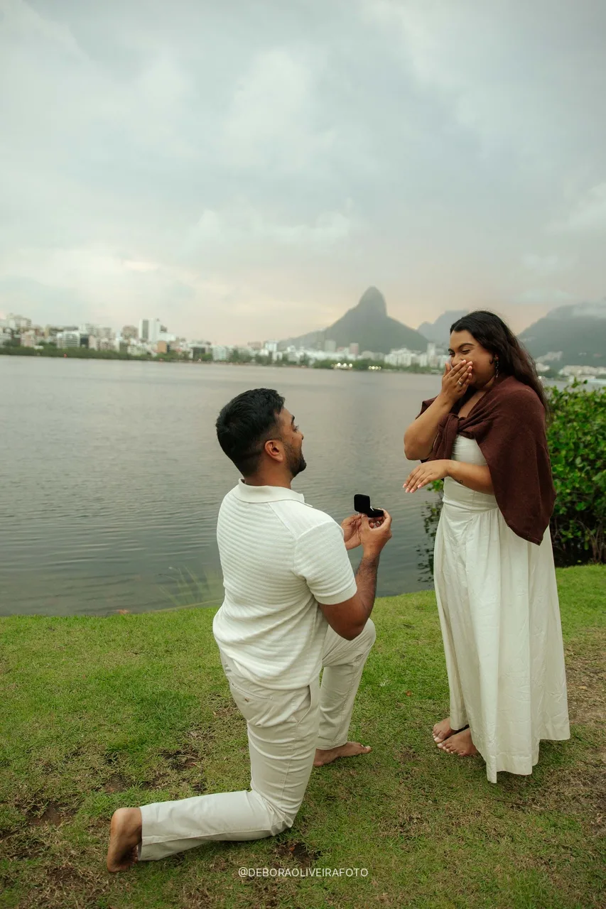 Naveen de joelho de novo na beira da água com o Dois Irmãos ao fundo