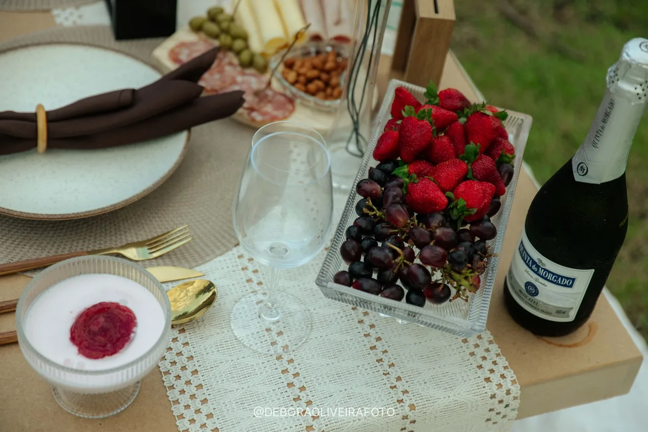 Frutas, espumante e louça na mesa do piquenique