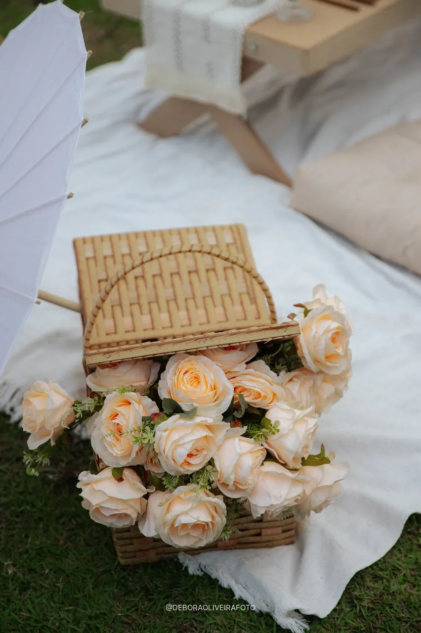 Cesta de rosas e sombrinha na toalha do piquenique