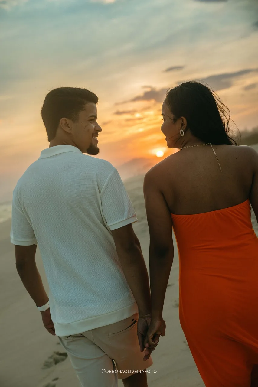 Engaged couple walking hand in hand toward the sunset