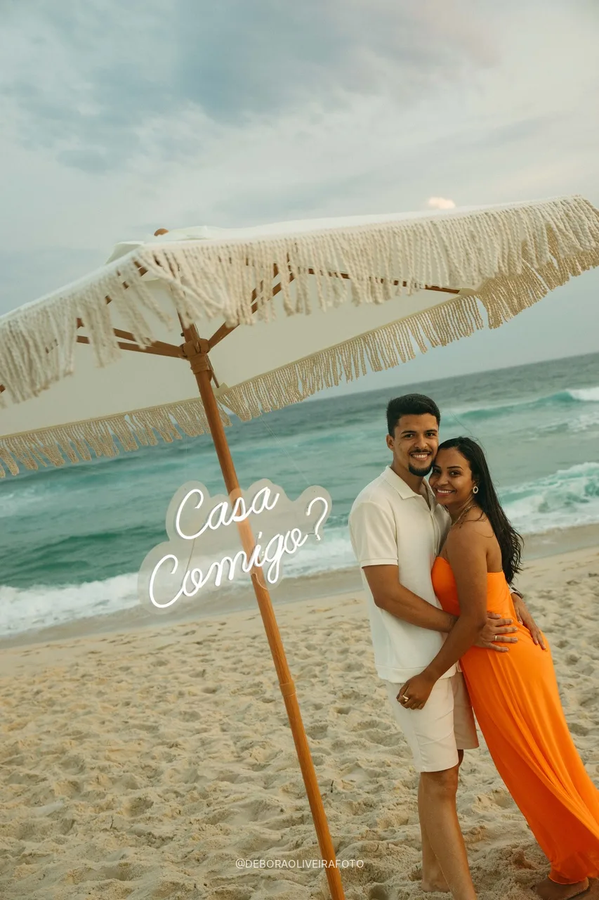 Engaged couple posing by the Casa Comigo sign on the beach