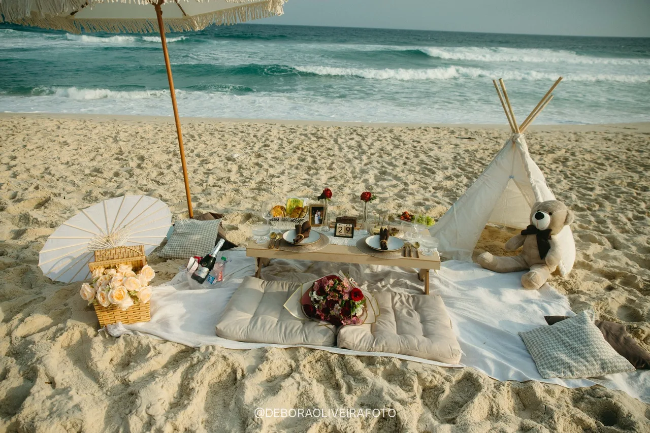 Picnic table, cushions, teepee and fringed umbrella on the sand