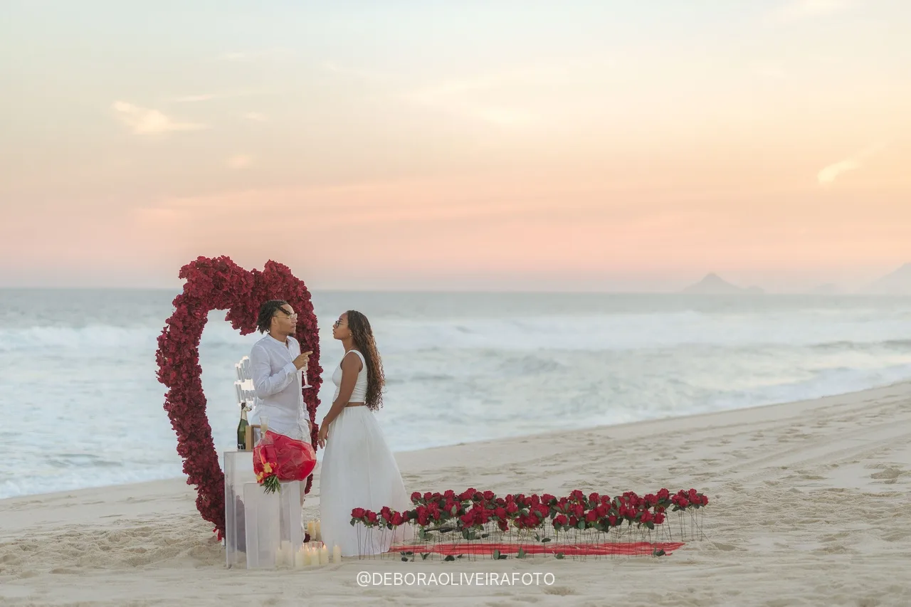 Vista amplia de la pareja y el corazón de rosas junto al mar
